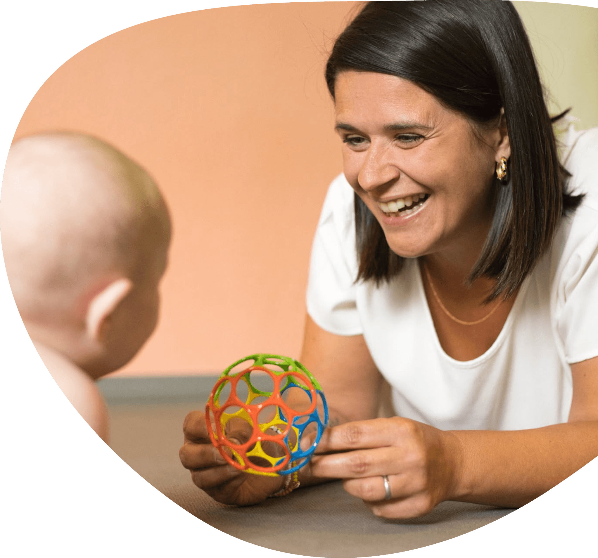 Eine lachende Frau mit dunklen Haaren spielt mit einem bunten Kugelspiel mit einem Baby.