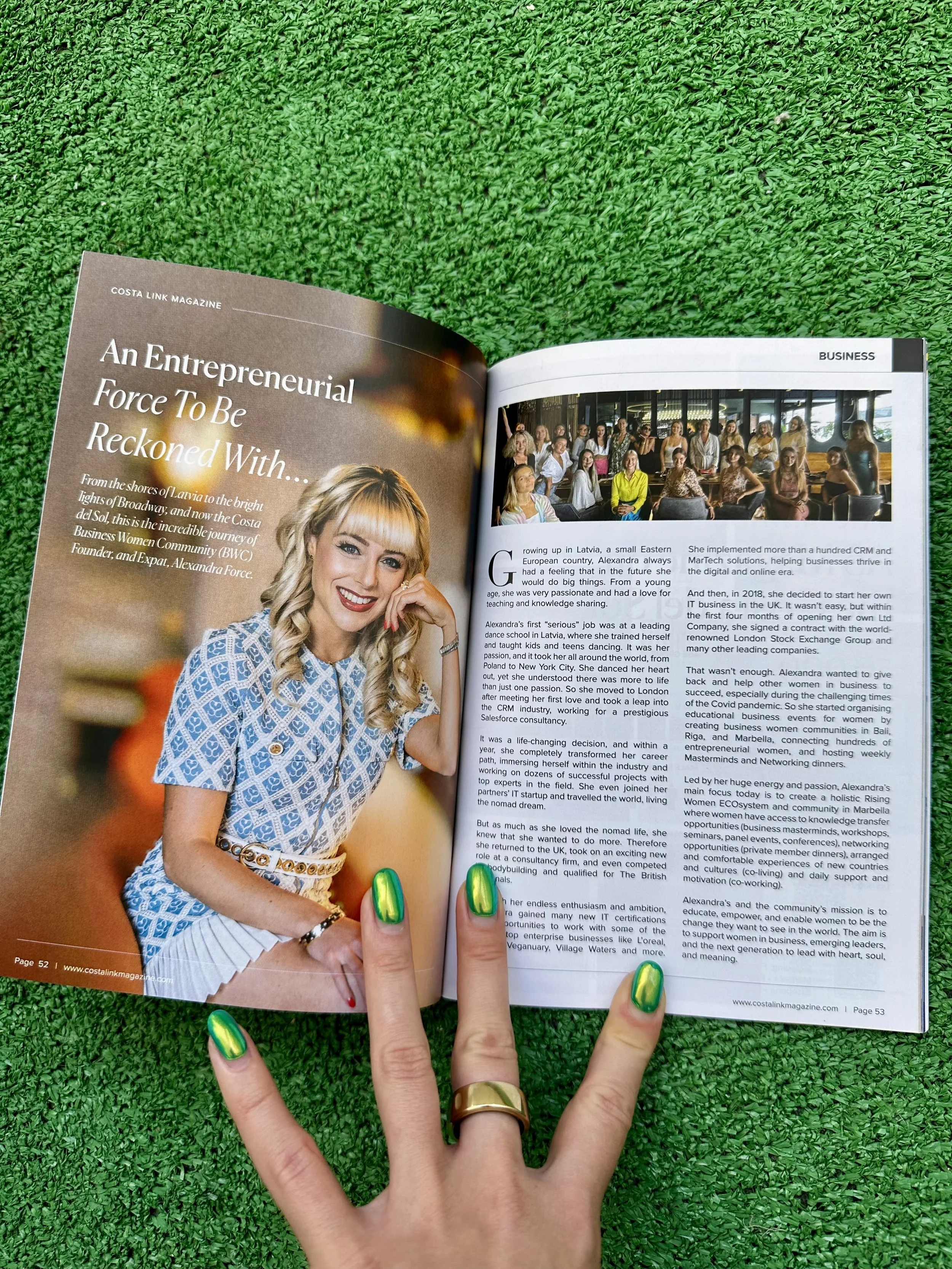 Open magazine on a green outdoor surface, showing an article titled 'An Entrepreneurial Force To Be Reckoned With' and a photo of a smiling woman with blonde hair wearing a blue patterned dress, a white belt, and jewelry.