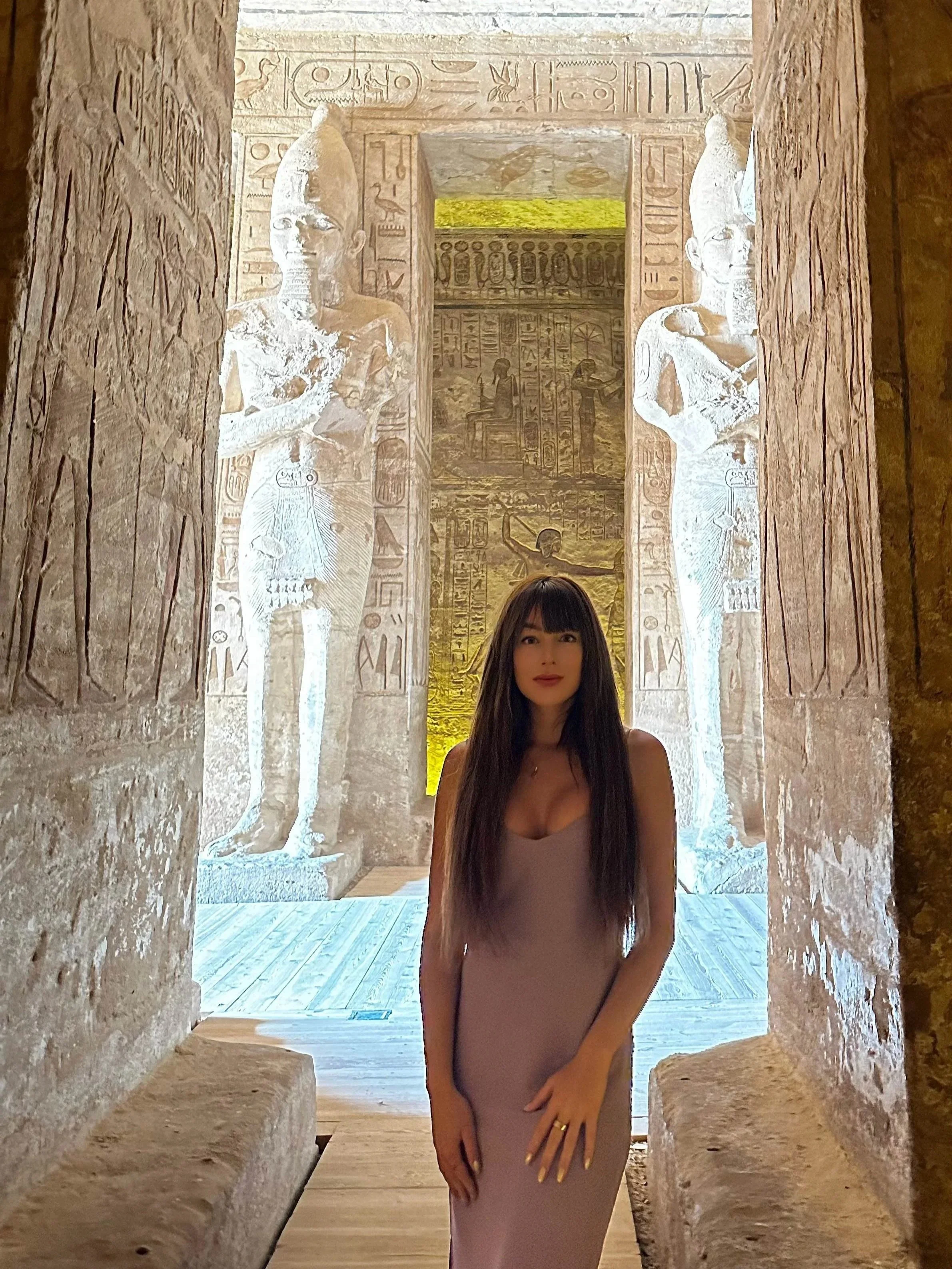 A woman standing in an ancient Egyptian temple, with hieroglyphics and carved statues in the background.