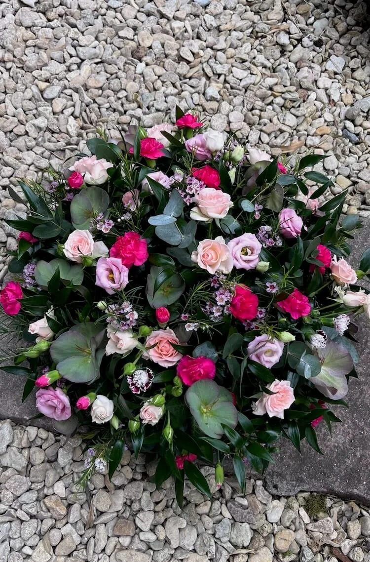 Vibrant floral posy arrangement featuring a variety of flowers and foliage in shades of hot pink, lilac, green and white, placed on a gravel surface