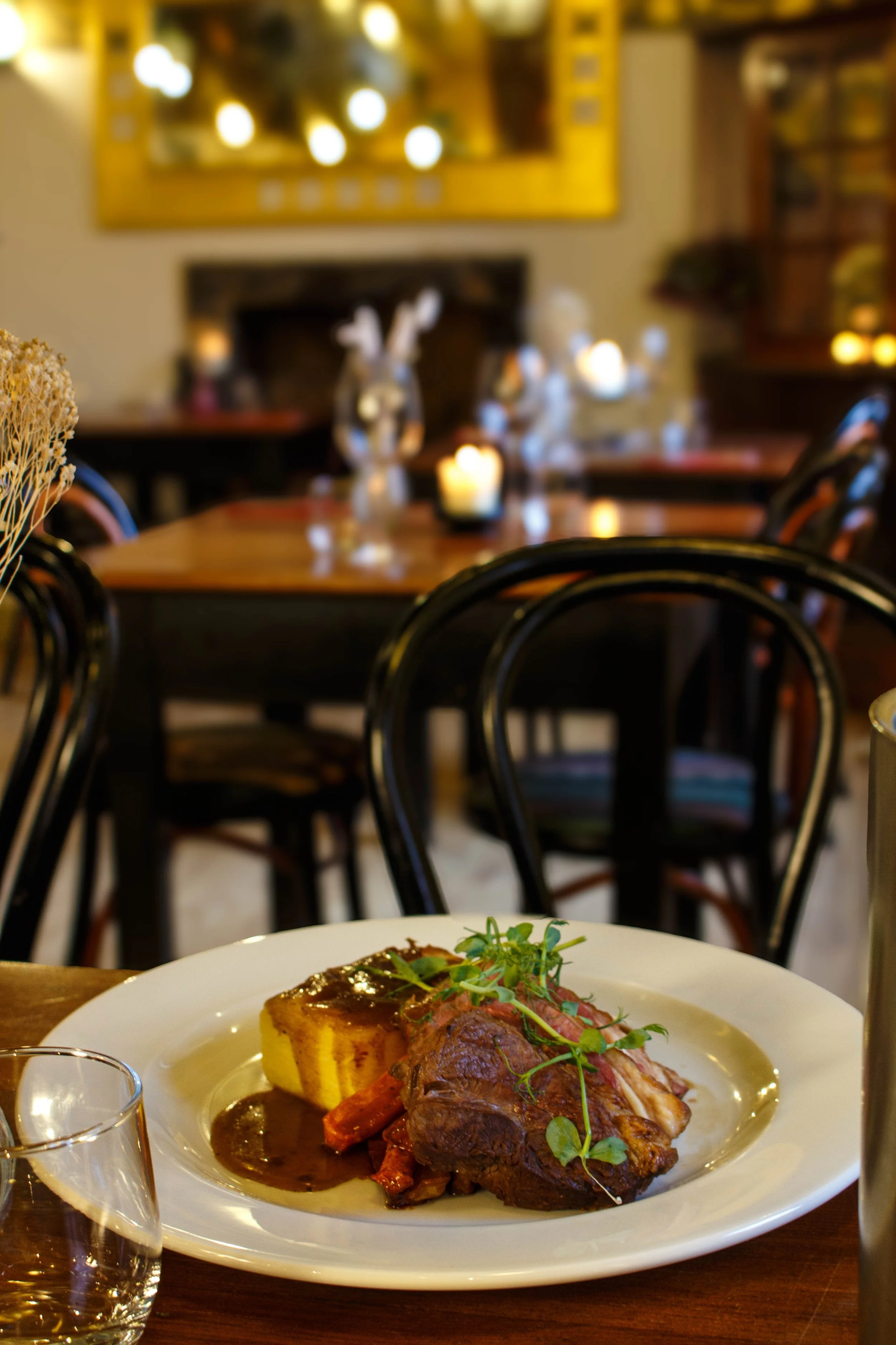 Plate of roasted meat with vegetables, garnished with herbs, on a white dish, set on a wooden dining table in a cozy restaurant.