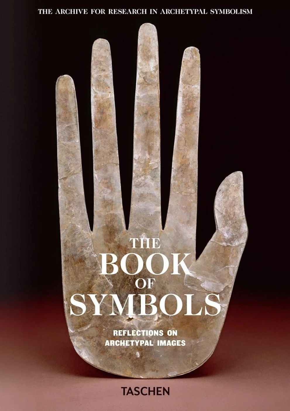 Book cover titled 'The Book of Symbols: Reflections on Archetypal Images', featuring an image of a stone hand sculpture with five fingers, on a dark background. Publisher: Taschen.