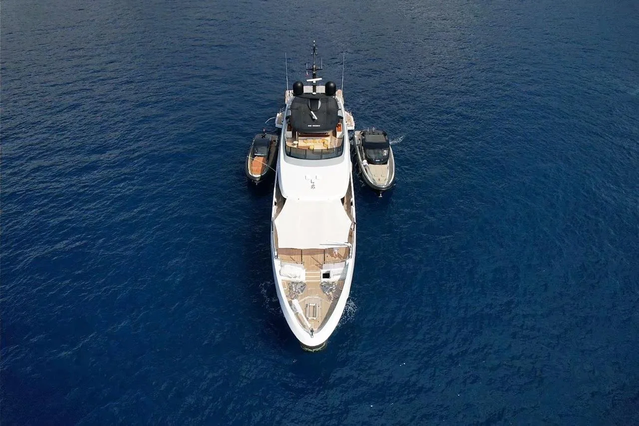 An aerial view of a large white yacht with two smaller boats attached on either side, floating on deep blue water.