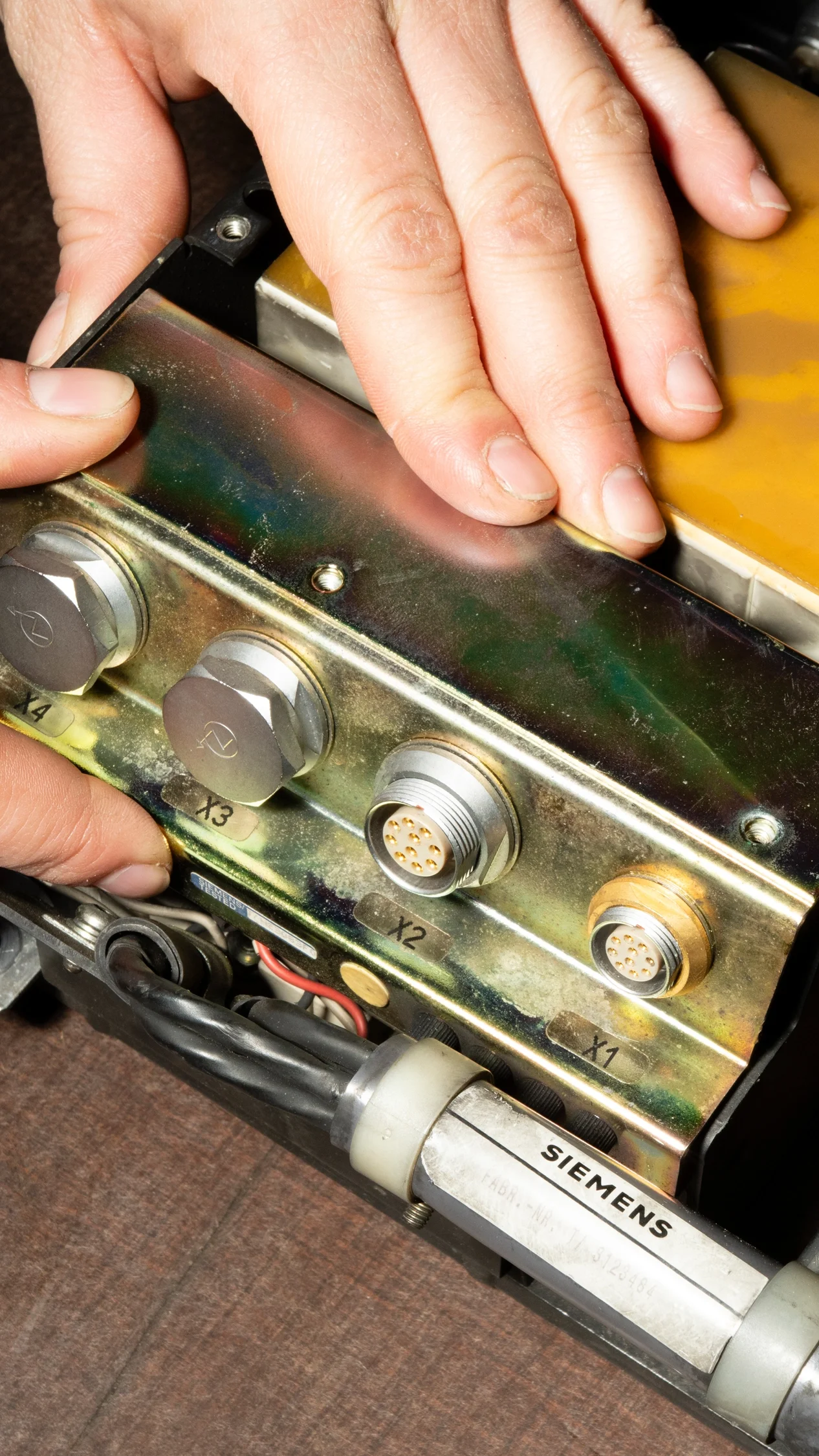 Eine Person hält ein elektronisches Bauteil mit mehreren Steckeranschlüssen in den Händen, vermutlich ein Teil eines technischen Geräts oder einer Maschine.