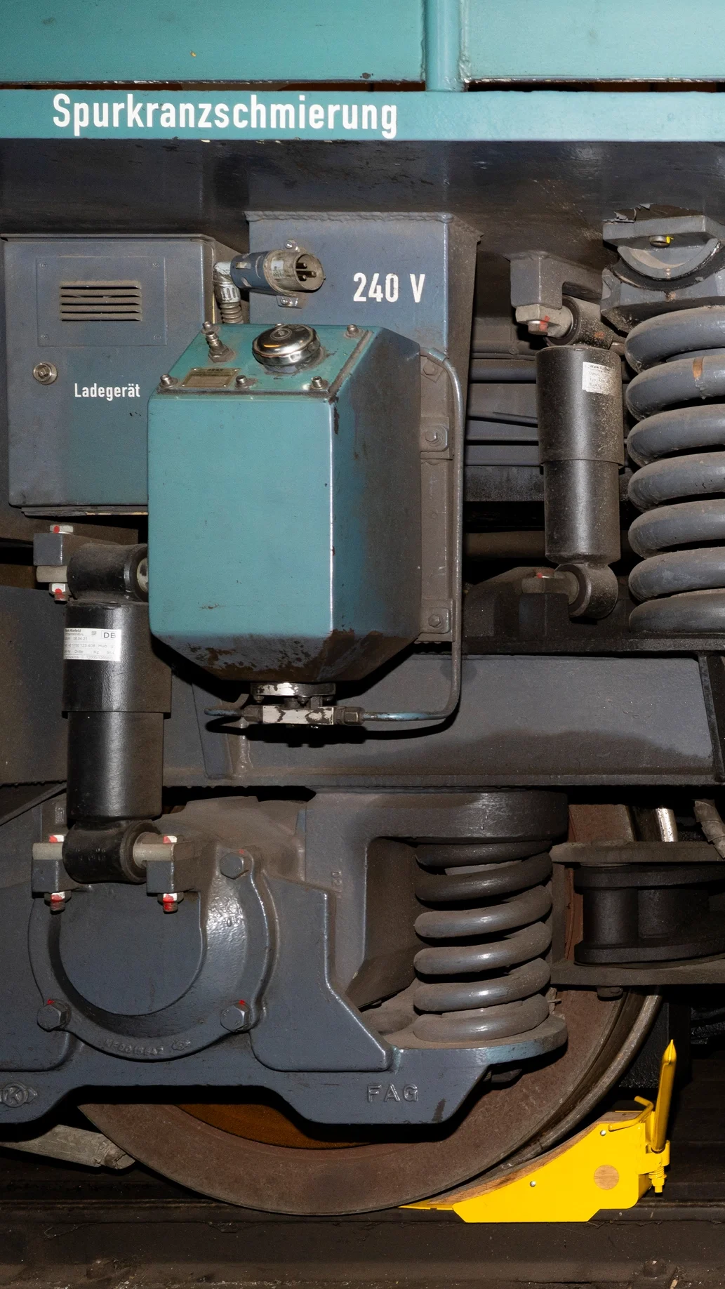 Nahaufnahme eines Eisenbahnfahrzeugs mit Wartungs- und Reparaturteilen, einschließlich einer großen Feder und einem Eisenbahnrad, mit Beschriftungen und technischem Equipment.