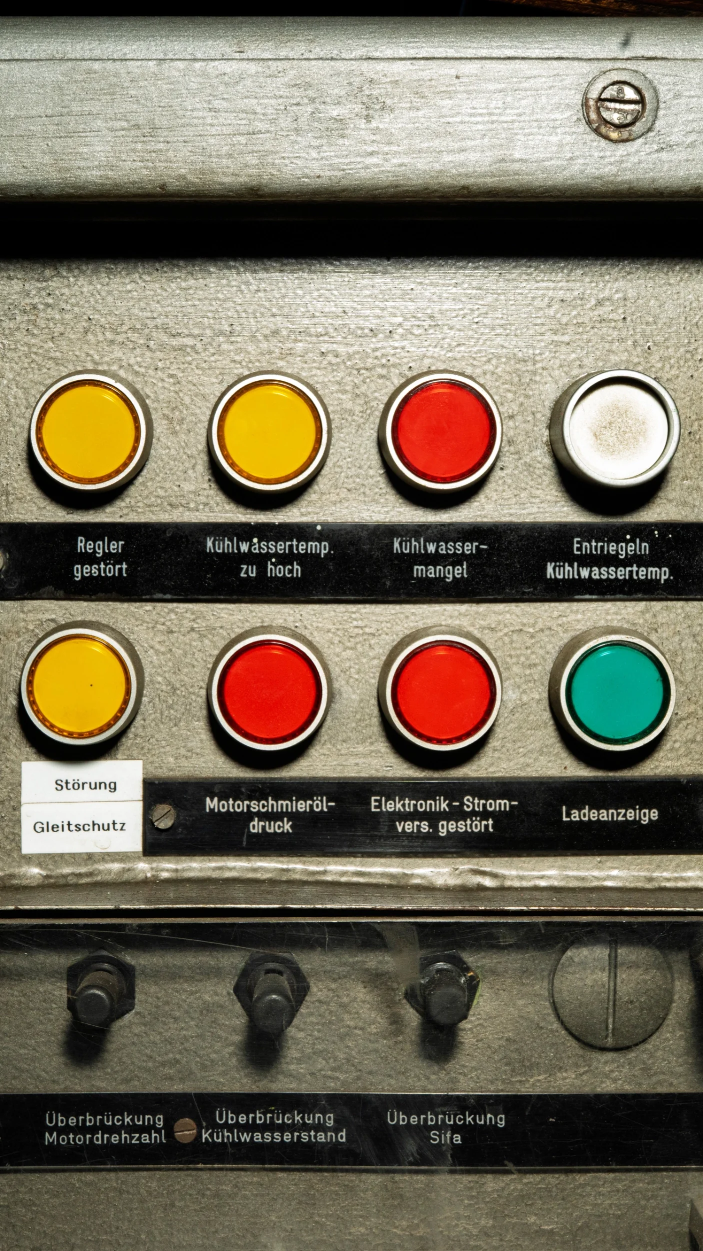 Betriebssteuerung mit mehreren roten, gelben und grünen Kontrollleuchten, Beschriftungen in Deutsch, Hinweise auf technische Störungen und Fehler im Zusammenhang mit Kühlwasser, Motoröl und Elektronik.