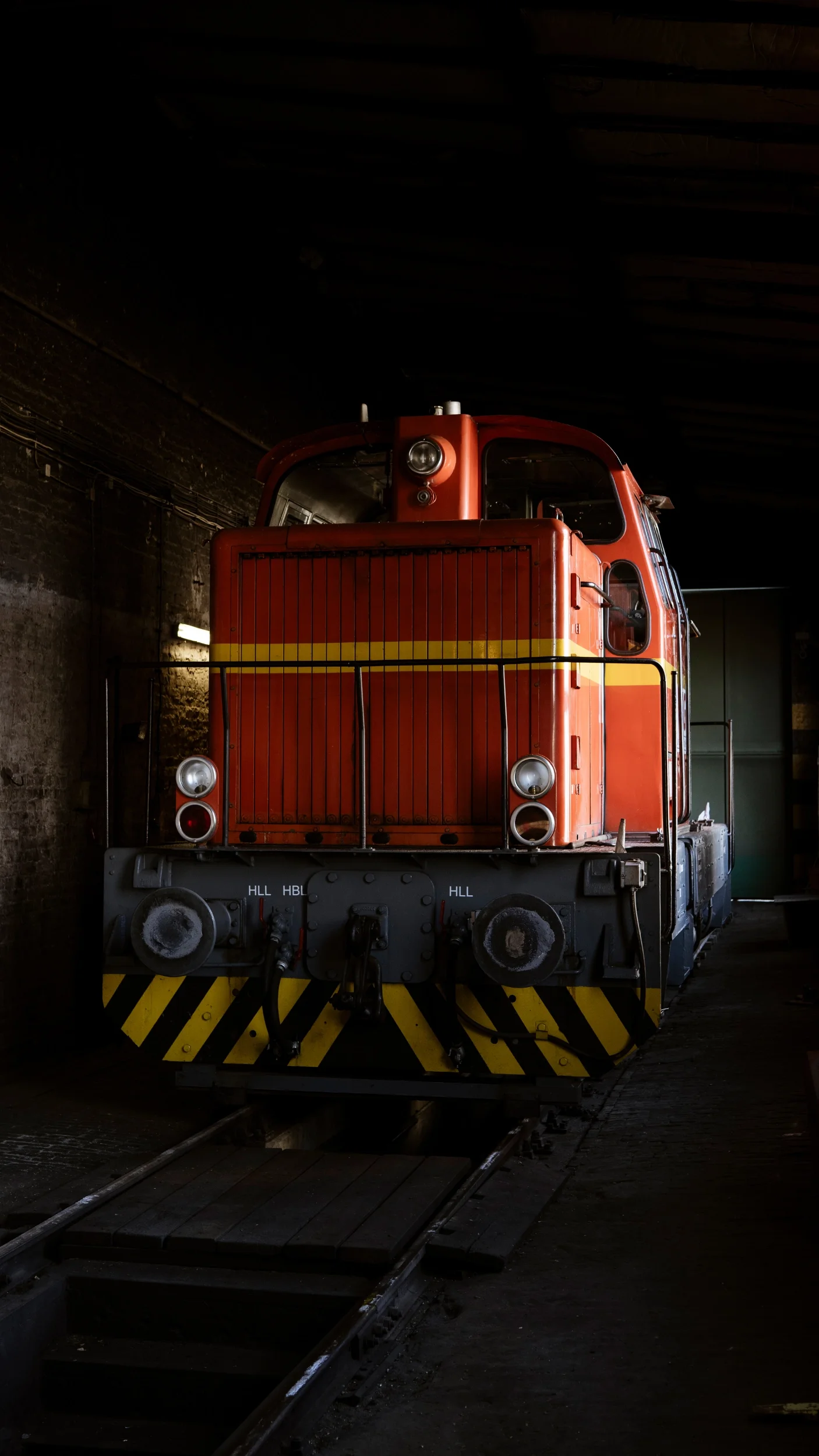 Ein rotes und gelbes Eisenbahnzug im Bahnhof. Der Zug steht auf Gleisen in einem dunklen, alten Schuppen.