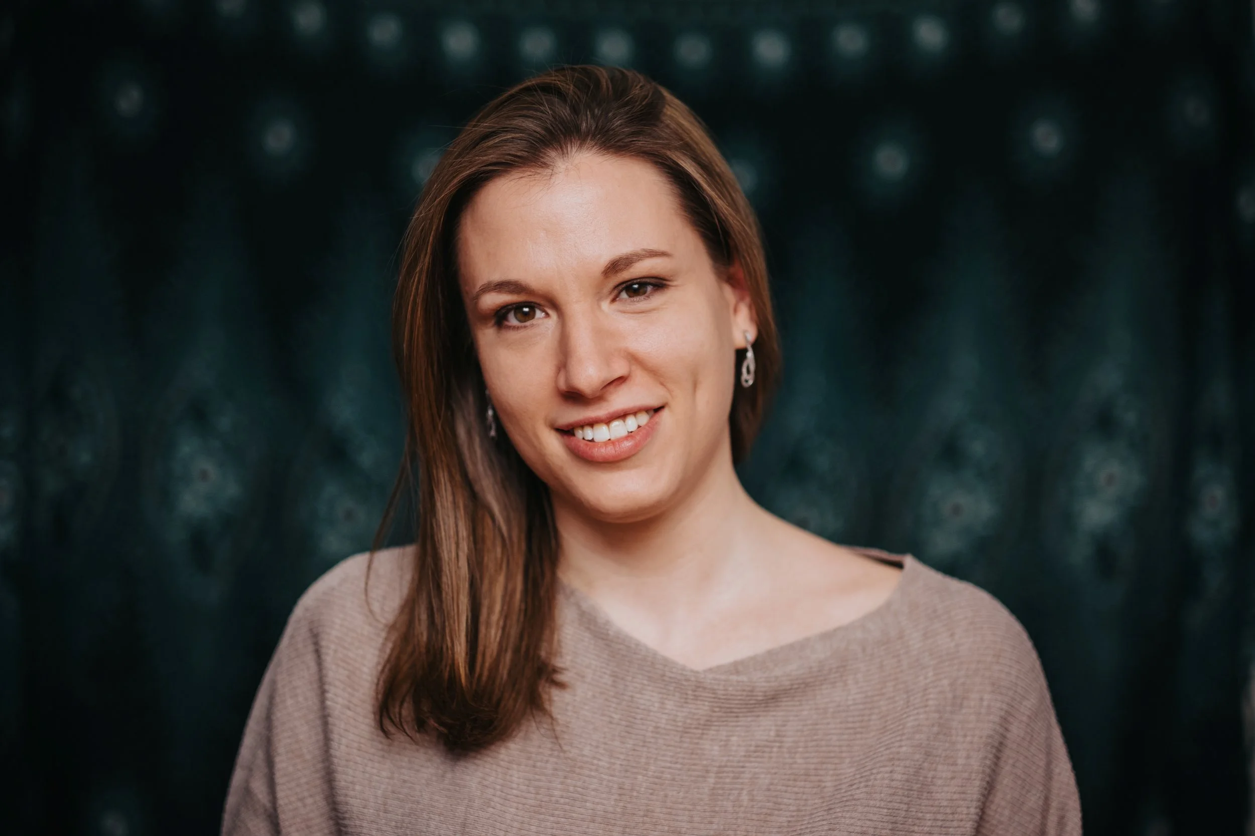 Ein Porträt von Svens Bodyworkpartnerin Adina, das sie lachend, mit braunen, glatten Haaren und einem Ohrring vor einem dunklen Hintergrund zeigt.