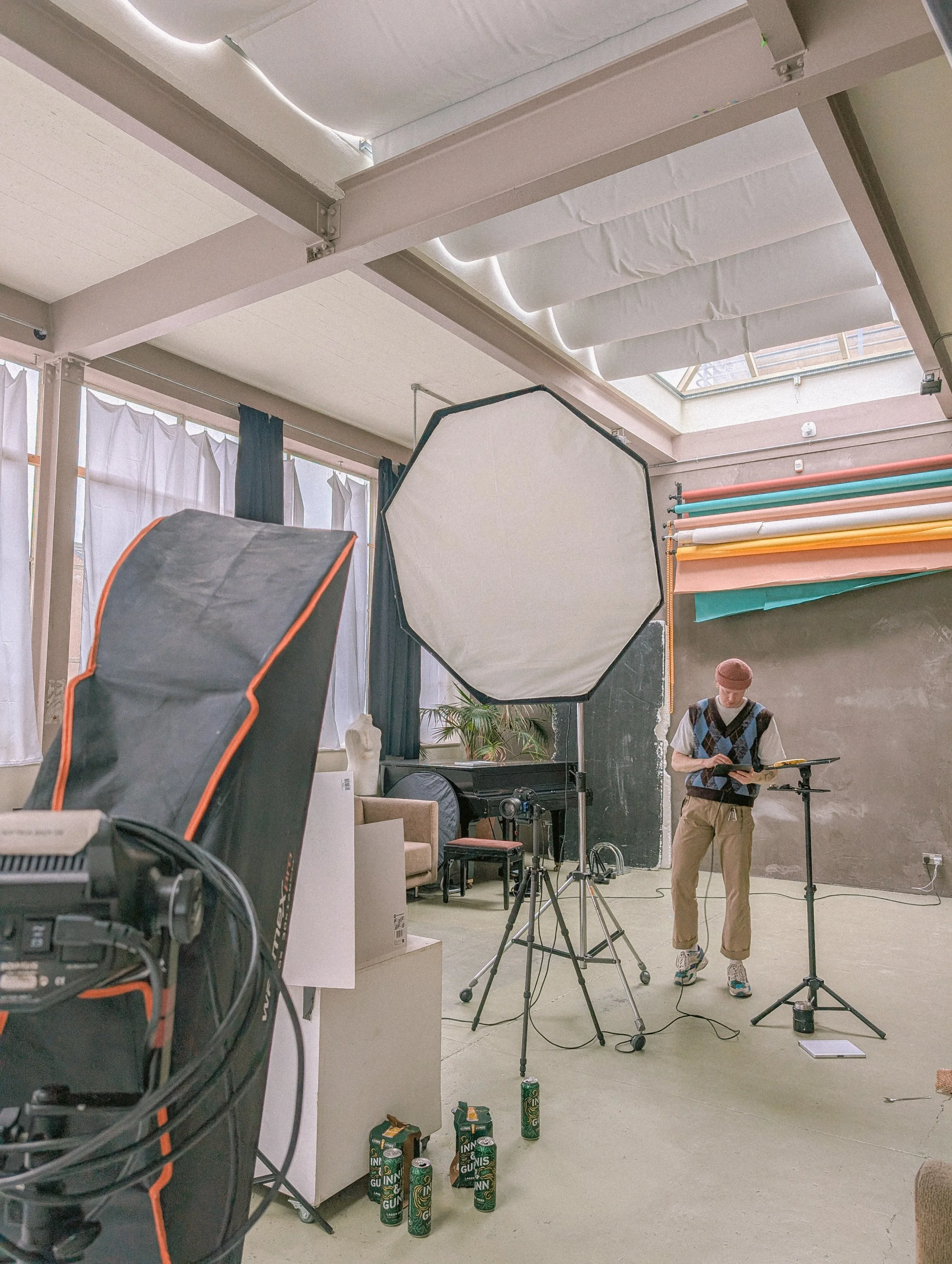 Studio setup with lighting equipment, softbox, backdrop, and person holding a tablet, in a photography or video production space.
