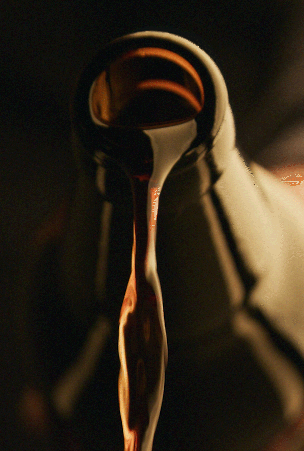 Close-up of a brown glass bottle pouring a dark liquid into a dark background.
