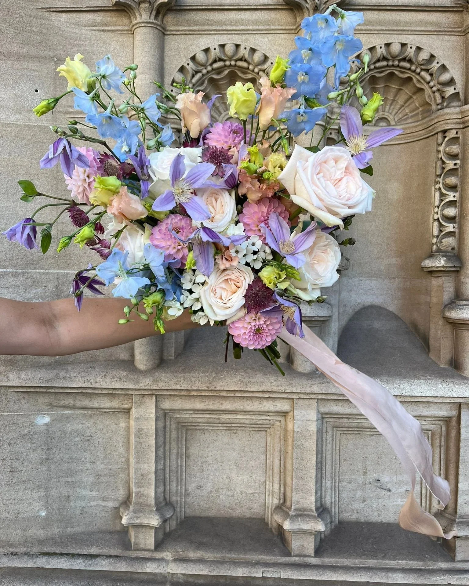 A person holding a colorful bouquet of flowers against a stone architectural background.