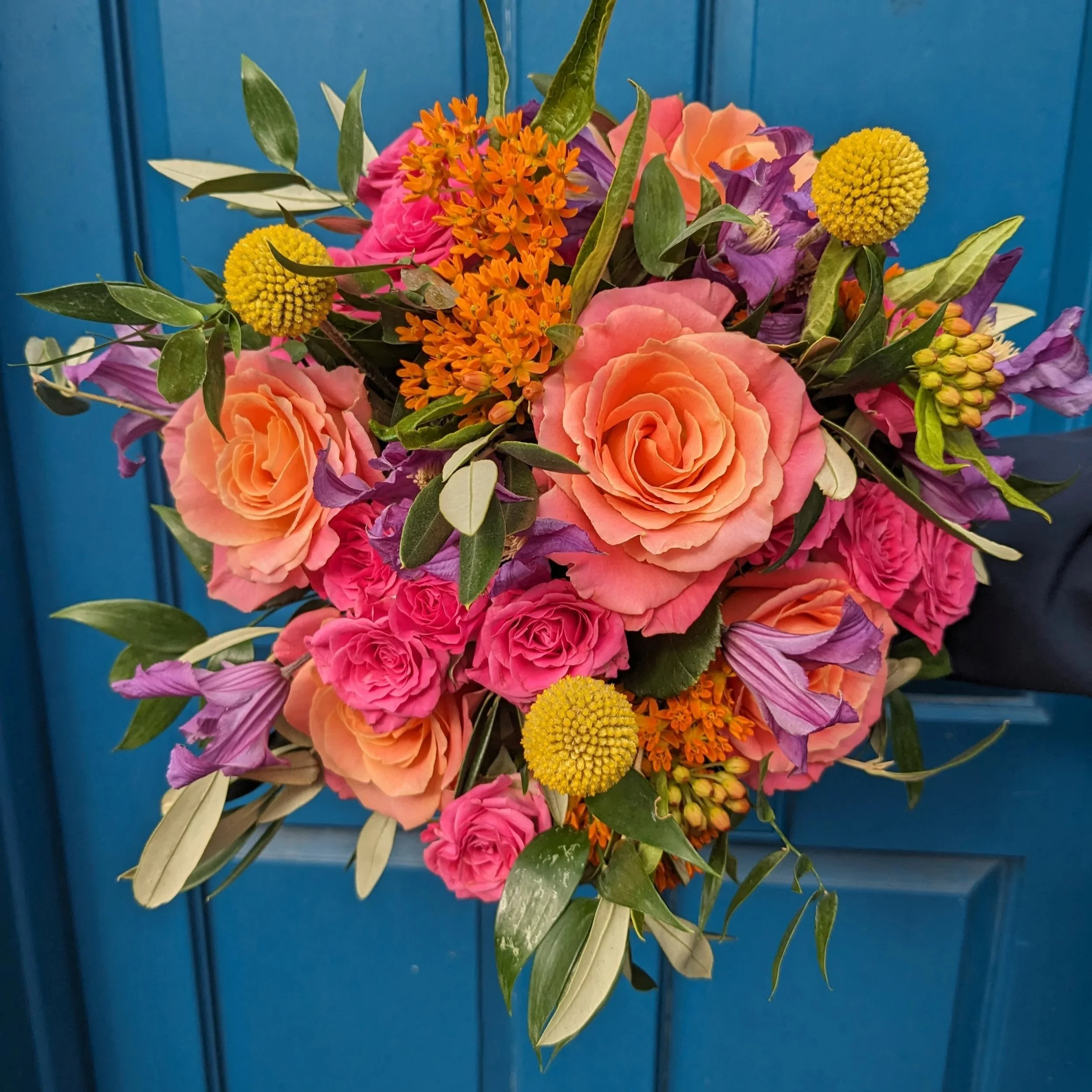 Colorful bouquet of pink, purple, orange, and yellow flowers with green leaves against a blue background.