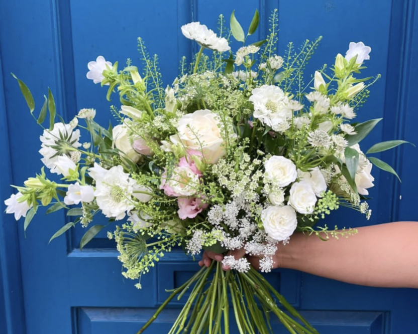 Person holding a bouquet of white and light pink flowers against a blue background.