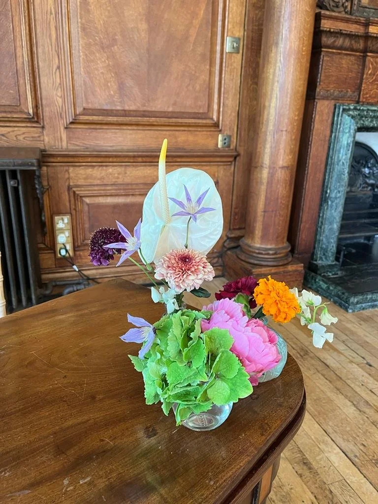 Colorful flower arrangement in glass vases on wooden table in a room with wooden walls and a fireplace.