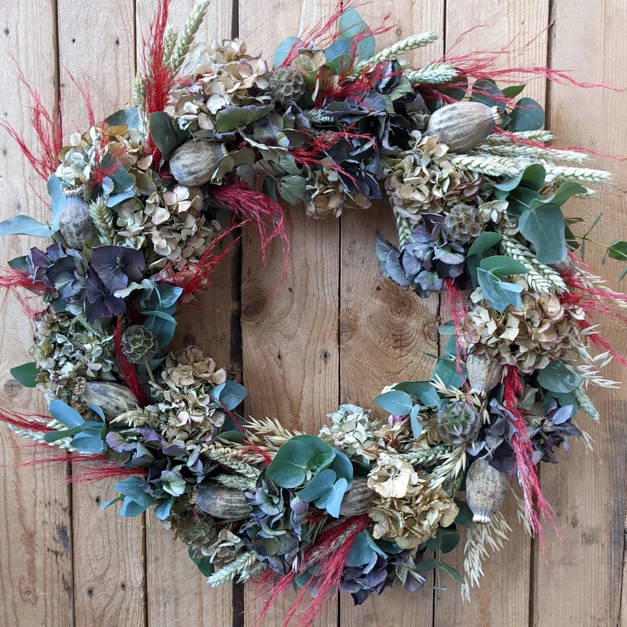 A floral wreath composed of dried hydrangeas, wheat, eucalyptus, and other dried plants on a wooden background.