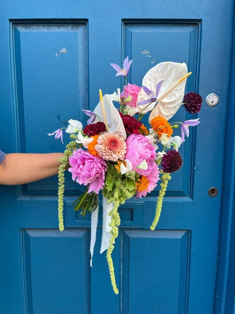 Hand holding a colorful floral bouquet in front of a blue door.