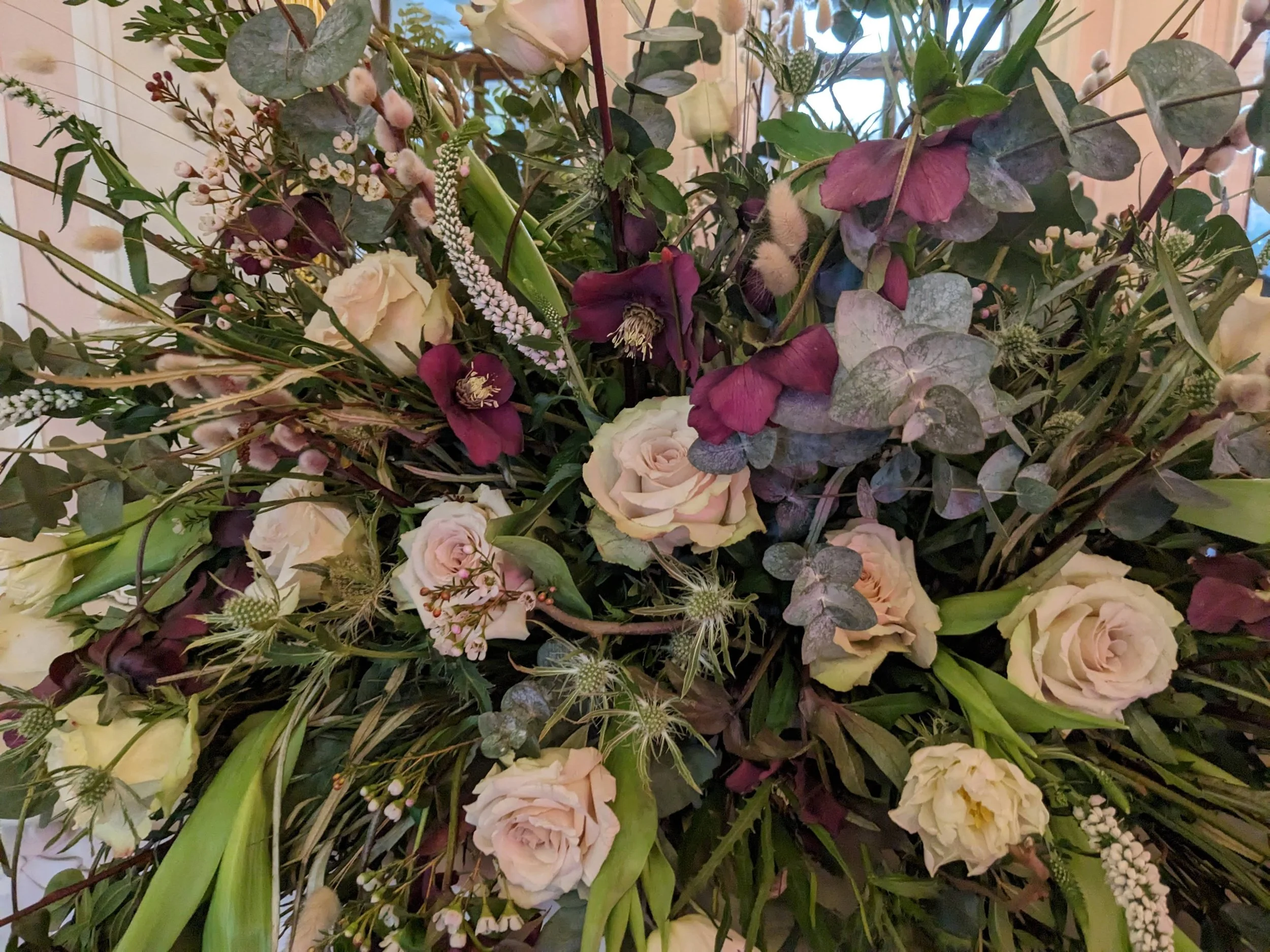 A Floral arrangement of mixed flowers including white roses, purple flowers, small white blooms, and various greenery with leaves and stems.