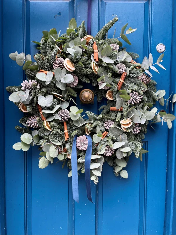 Decorative holiday wreath with pinecones, cinnamon and eucalyptus leaves hanging on a blue door.