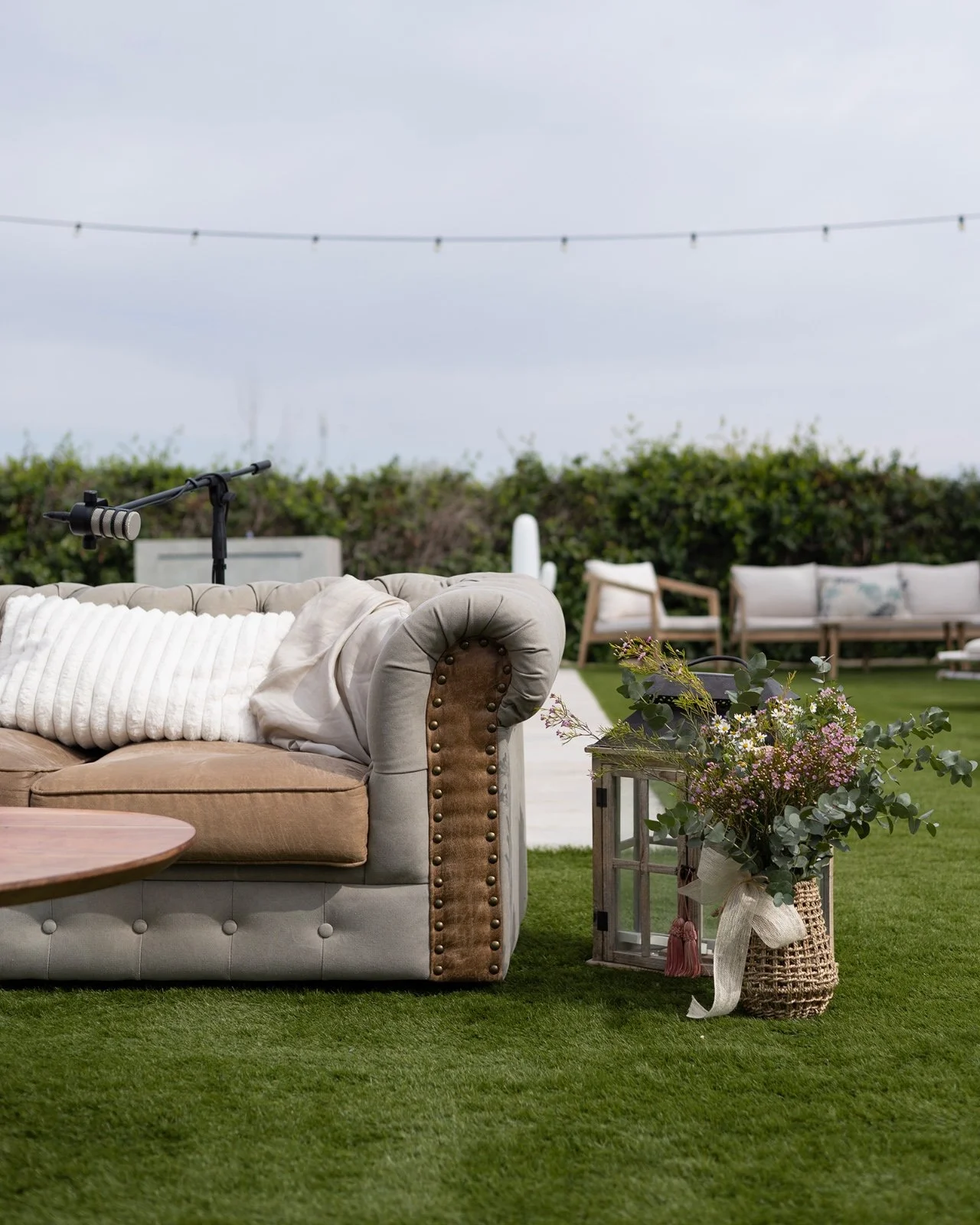 Sofá de estilo clásico con cojín en un espacio al aire libre decorado con plantas y muebles de jardín, en un día nublado.