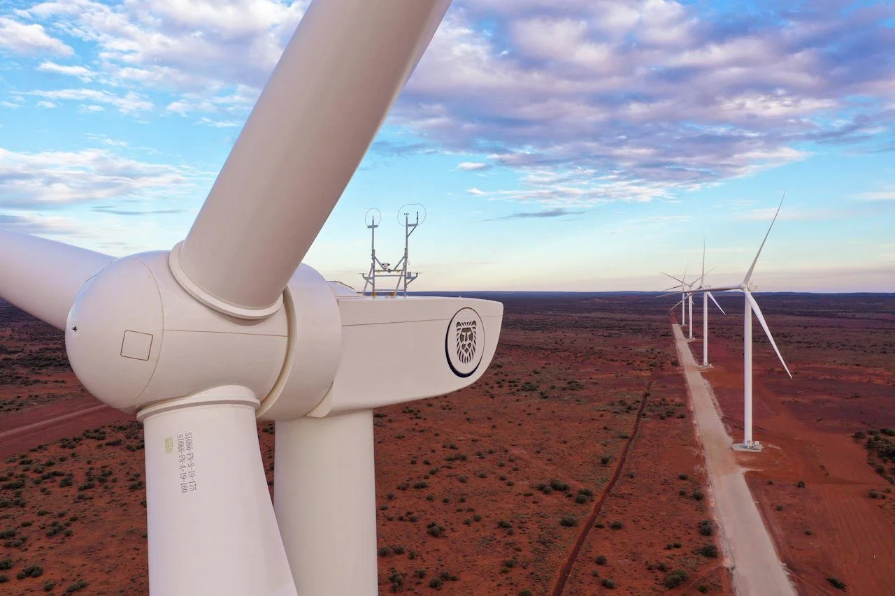 A distant view of wind turbines in a red desert landscape with a cloudy sky.