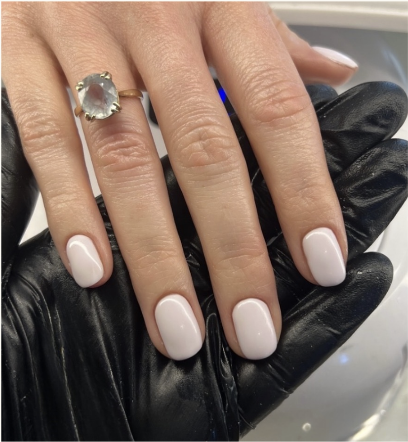A hand with white manicured nails wearing a large gemstone ring on the ring finger, held by a gloved hand.