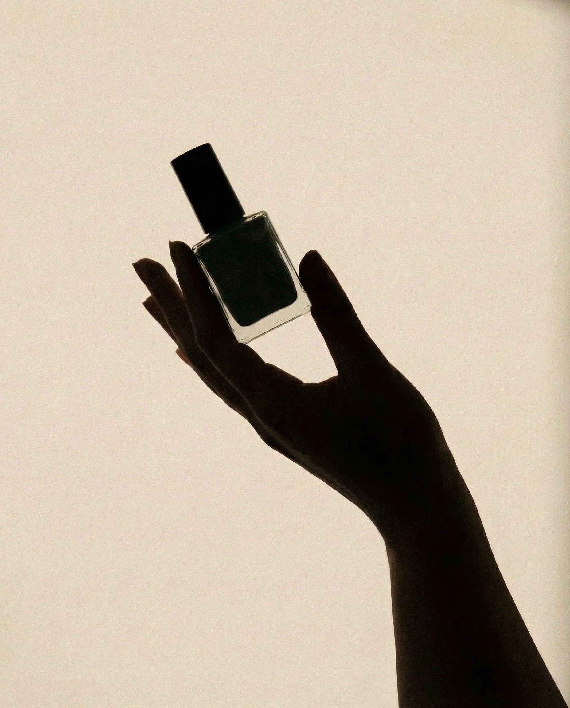 Silhouette of a hand holding a nail polish bottle against a plain background.