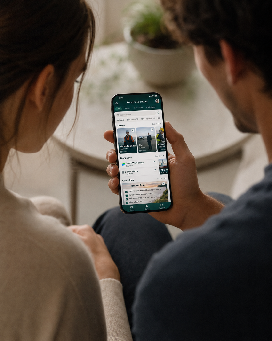 A young man and woman sitting together, looking at a smartphone screen that displays a career planning app called 'Future Vision Board', with sections for careers, companies, and aspirations.