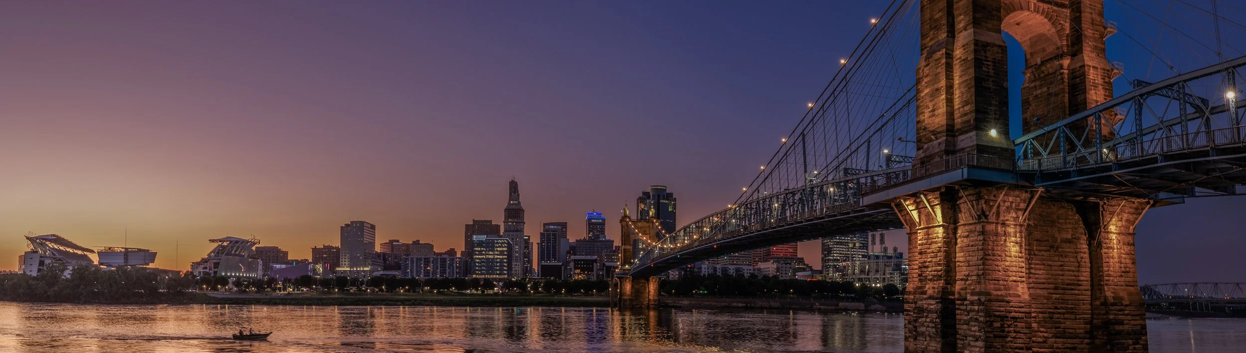 Twilight photograph of downtown Cincinnati, the Roebling bridge and the riverfront.
