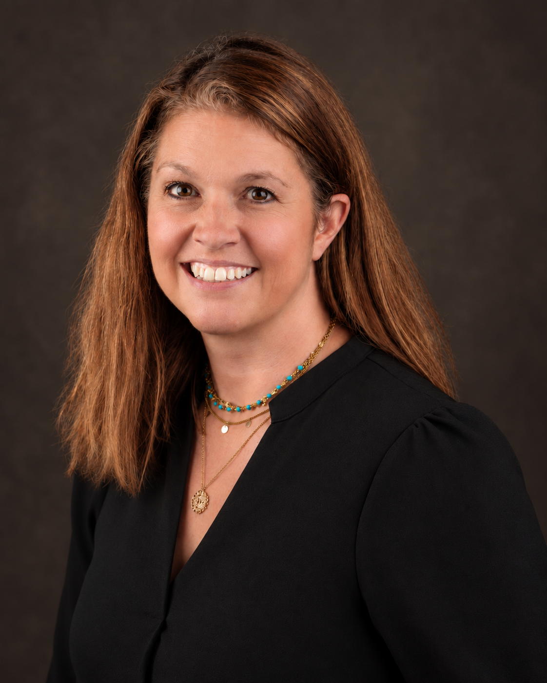 Professional studio portrait of a woman in a black blouse against a dark neutral background.