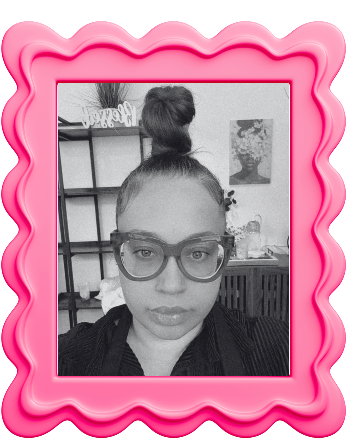 Black and white photo of a person with glasses and a high bun hairstyle, sitting indoors with shelves and artwork in the background, surrounded by a pink neon frame.