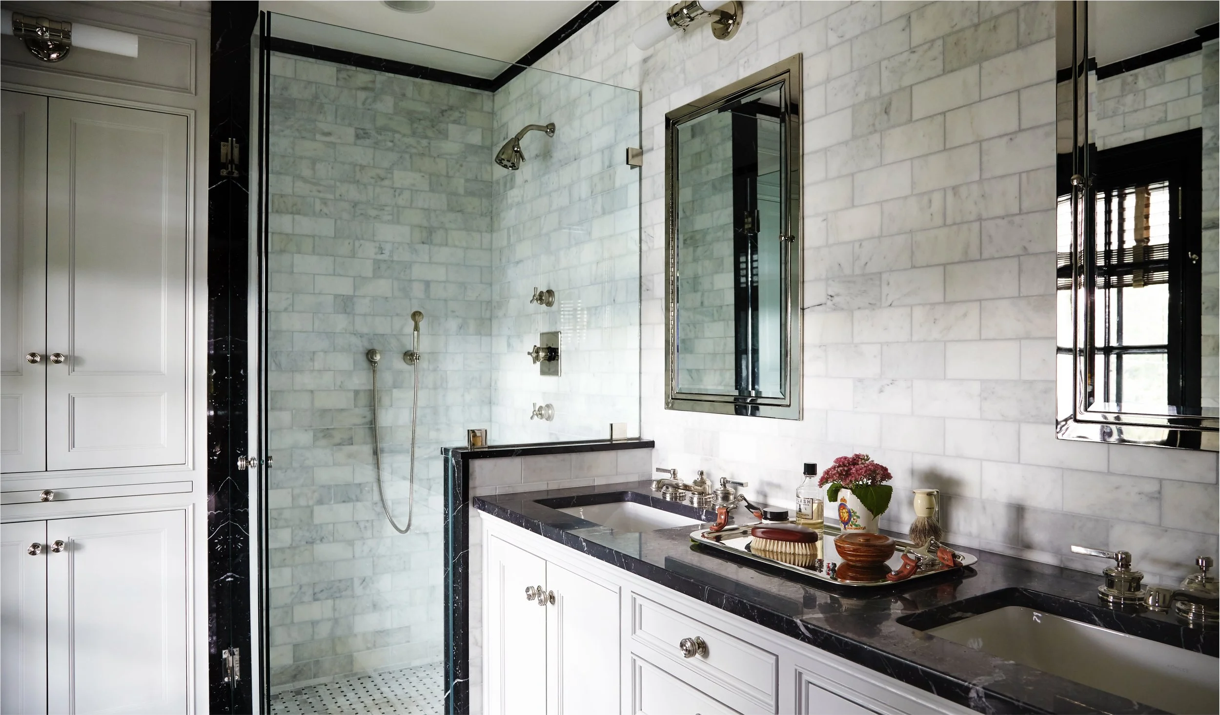 Bathroom with white marble walls, a glass shower with chrome fixtures, a black granite countertop sink, and a mirror with a silver frame.