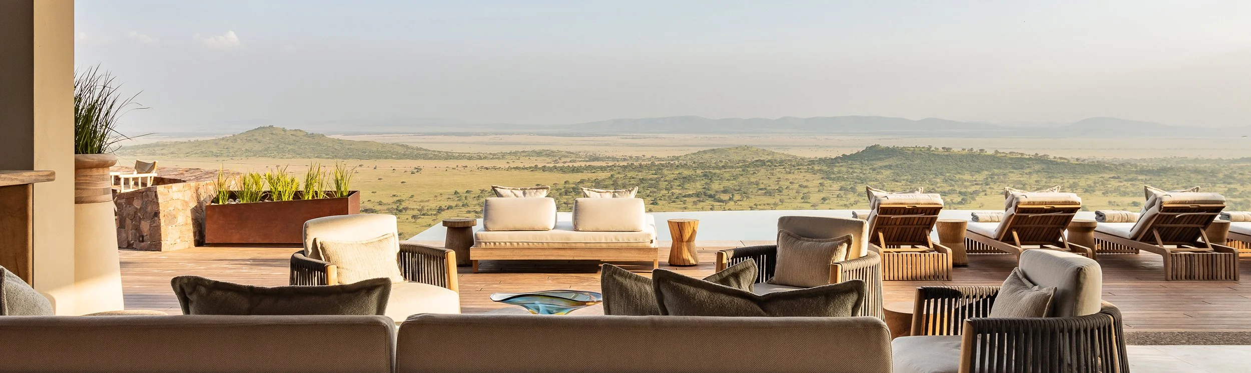 Luxury outdoor seating area with couches and chairs overlooking a vast landscape of plains, hills, and distant mountains.
