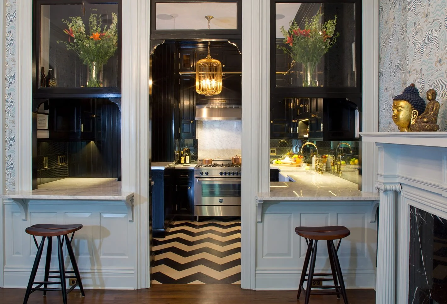 View of a kitchen through a pass-through with bar stools, black cabinets, marble countertops, and decorative Buddha statues.