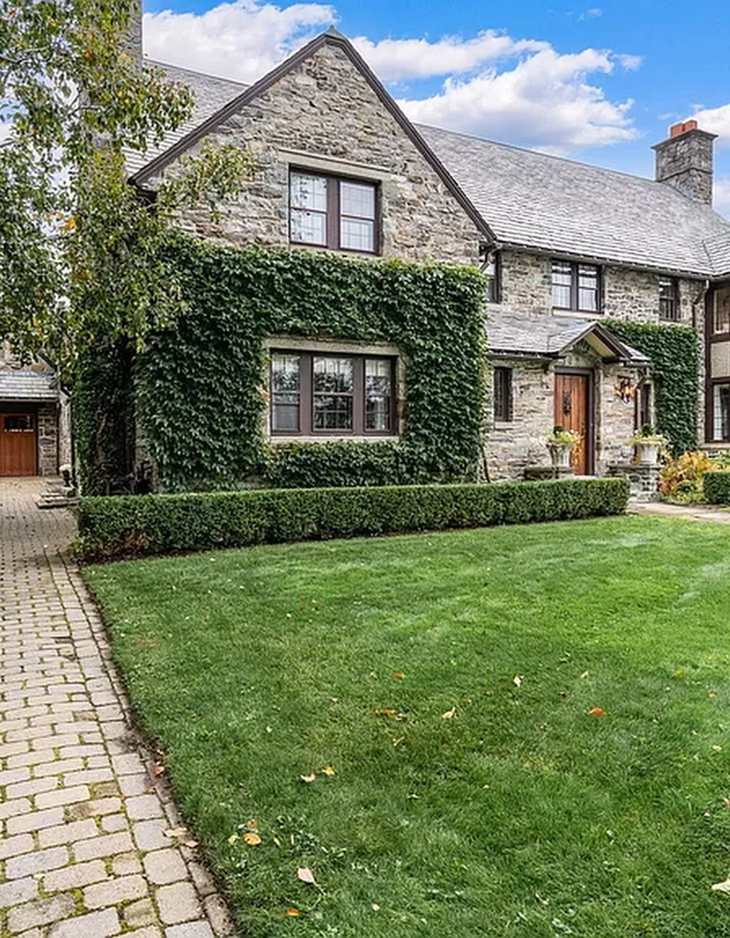 Stone house with ivy-covered walls, a wooden front door, and a well-kept green lawn in front.