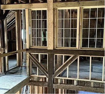 Interior of a wooden building under construction with exposed framing and large windows.