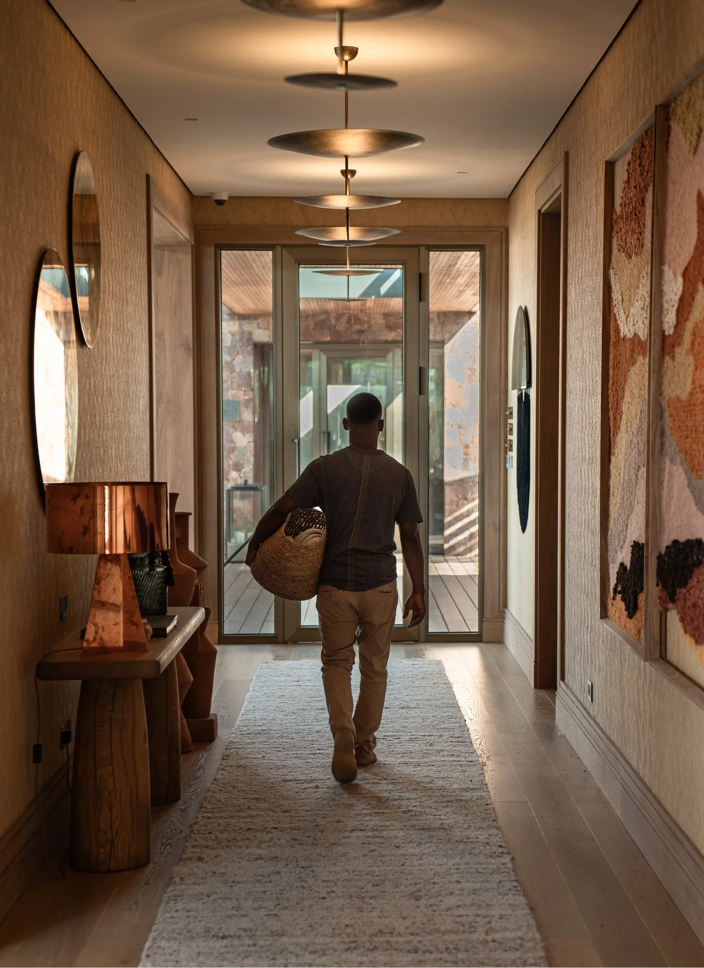 A man walking into a house holding a woven basket, with glass doors and a wooden deck outside.