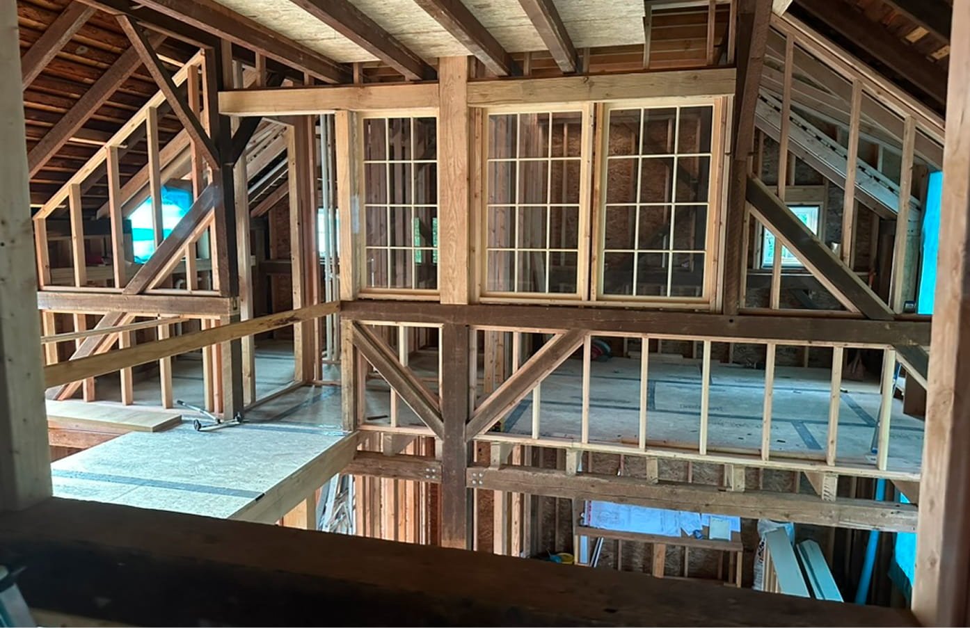 Interior view of a house under construction, showing wooden framing, walls, and windows in the process of being built.