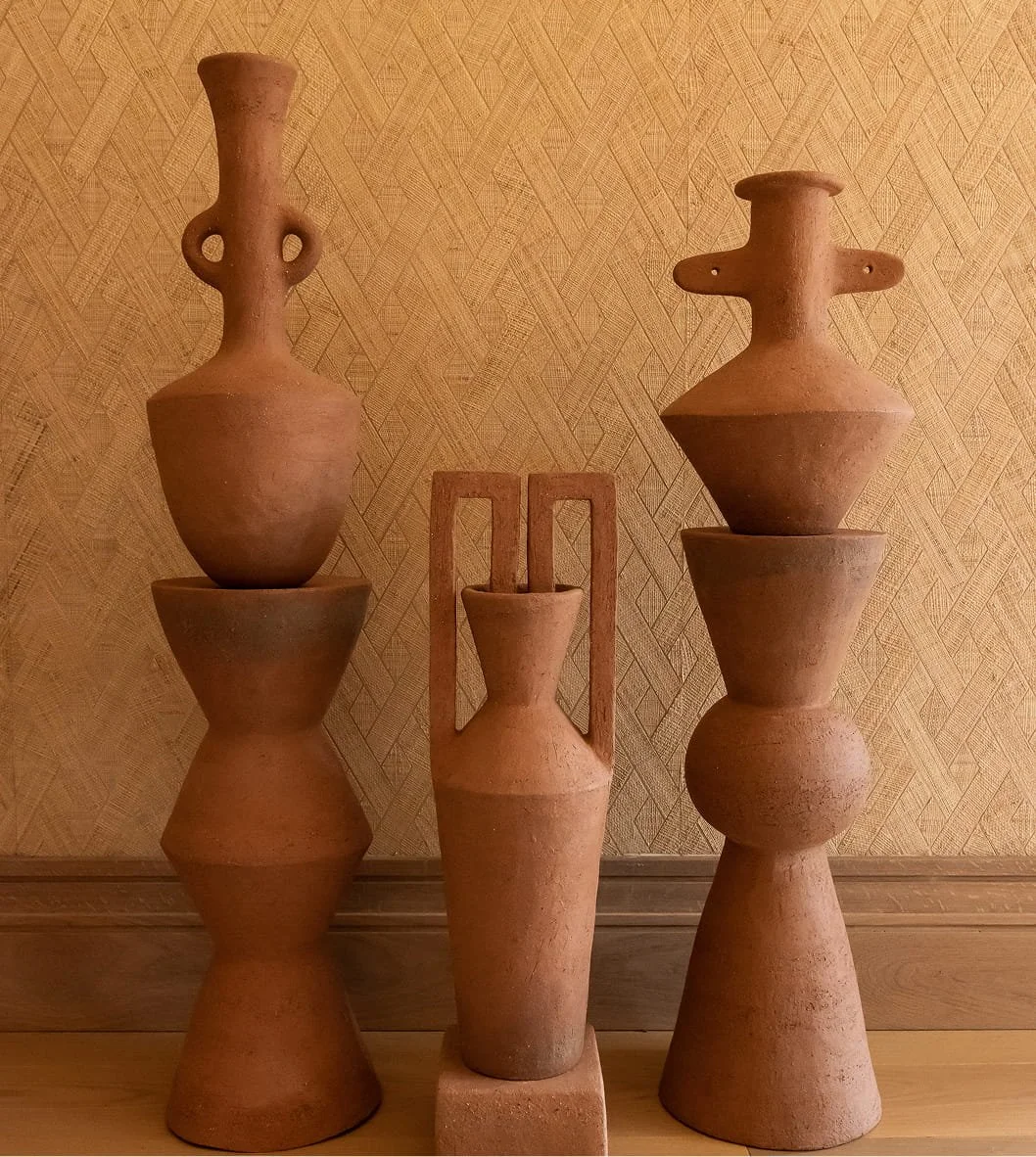 Collection of five terracotta vases with geometric shapes on a wooden surface against a textured, yellowish wall.