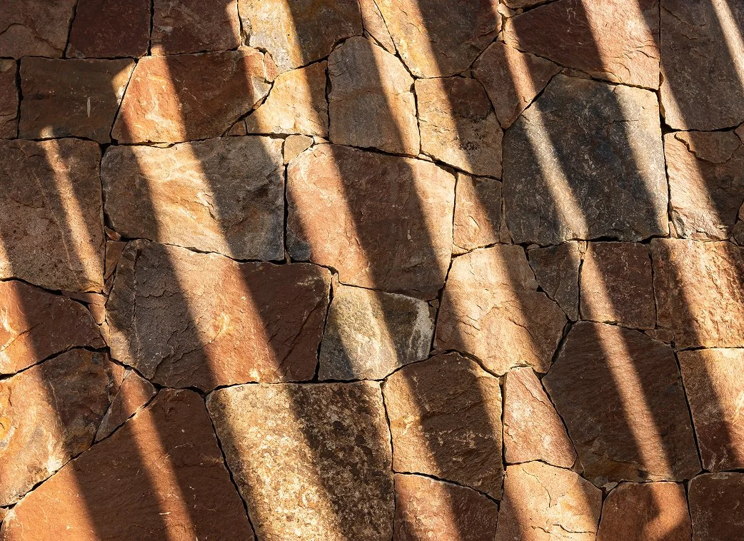 Sunlight casting diagonal shadows on a textured red brick wall.
