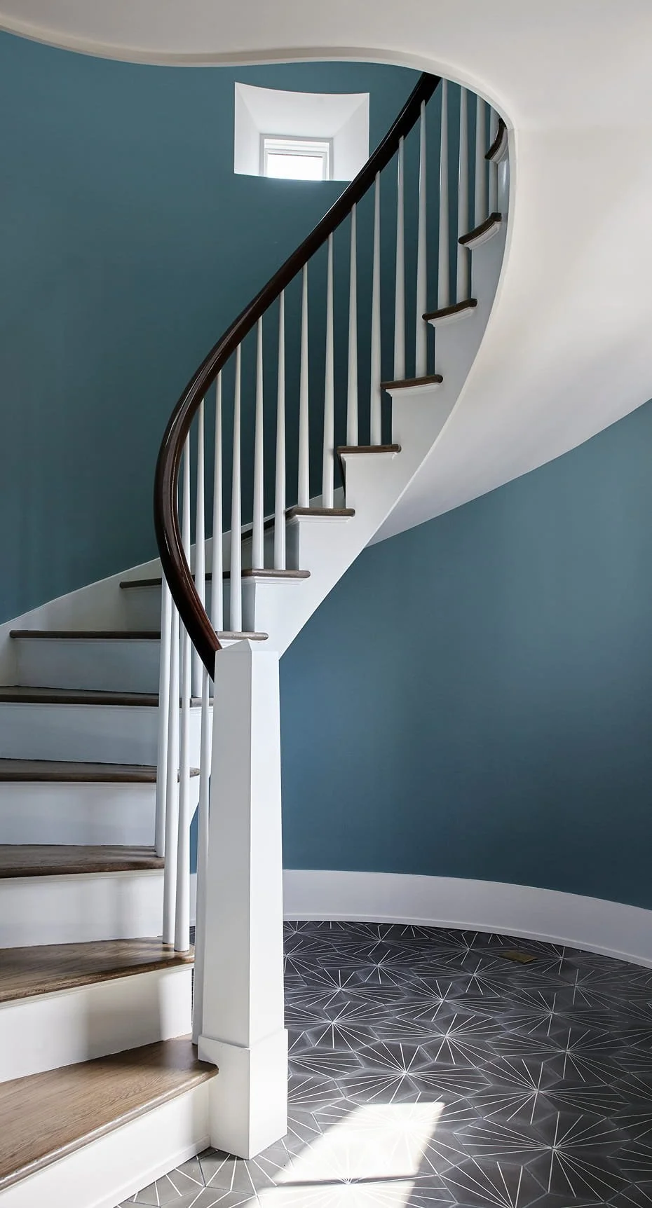 Interior staircase with white risers, wooden treads, white spindles, dark wooden handrail, blue wall, and geometric patterned floor.