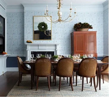 Elegant dining room with a large wooden table, eight upholstered chairs, a white fireplace, a chandelier, a cabinet with plants, and a mirror on the wall.