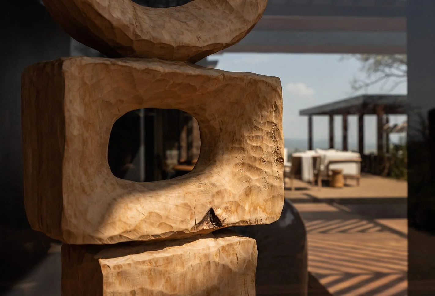 Close-up of a carved wooden sculpture with a hollow center, with an outdoor patio and seating area visible in the background.