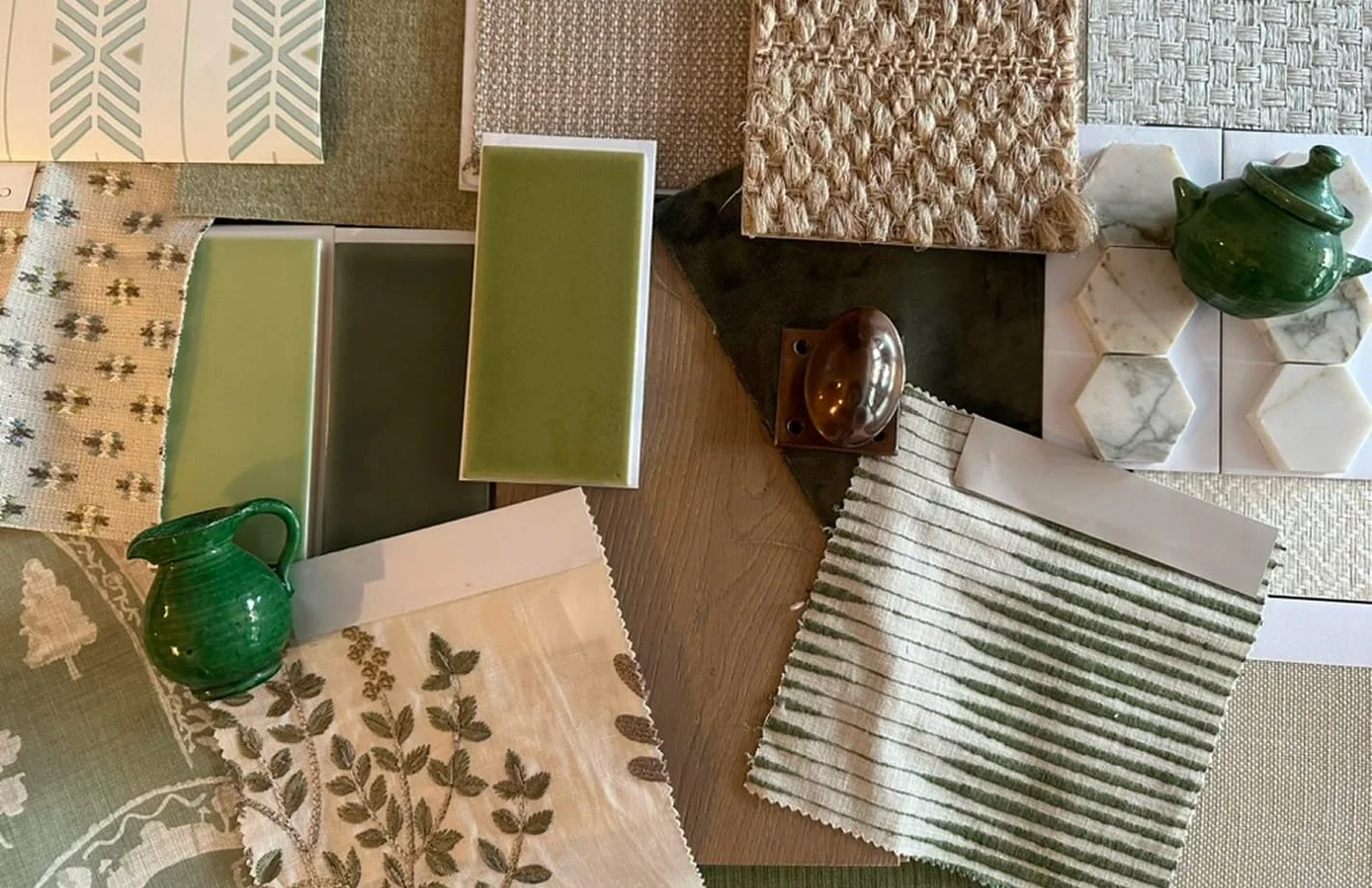 Arrangement of fabric swatches, tableware, and decorative items on a table, including green teapots, marble tiles, woven textiles, and wood surfaces.