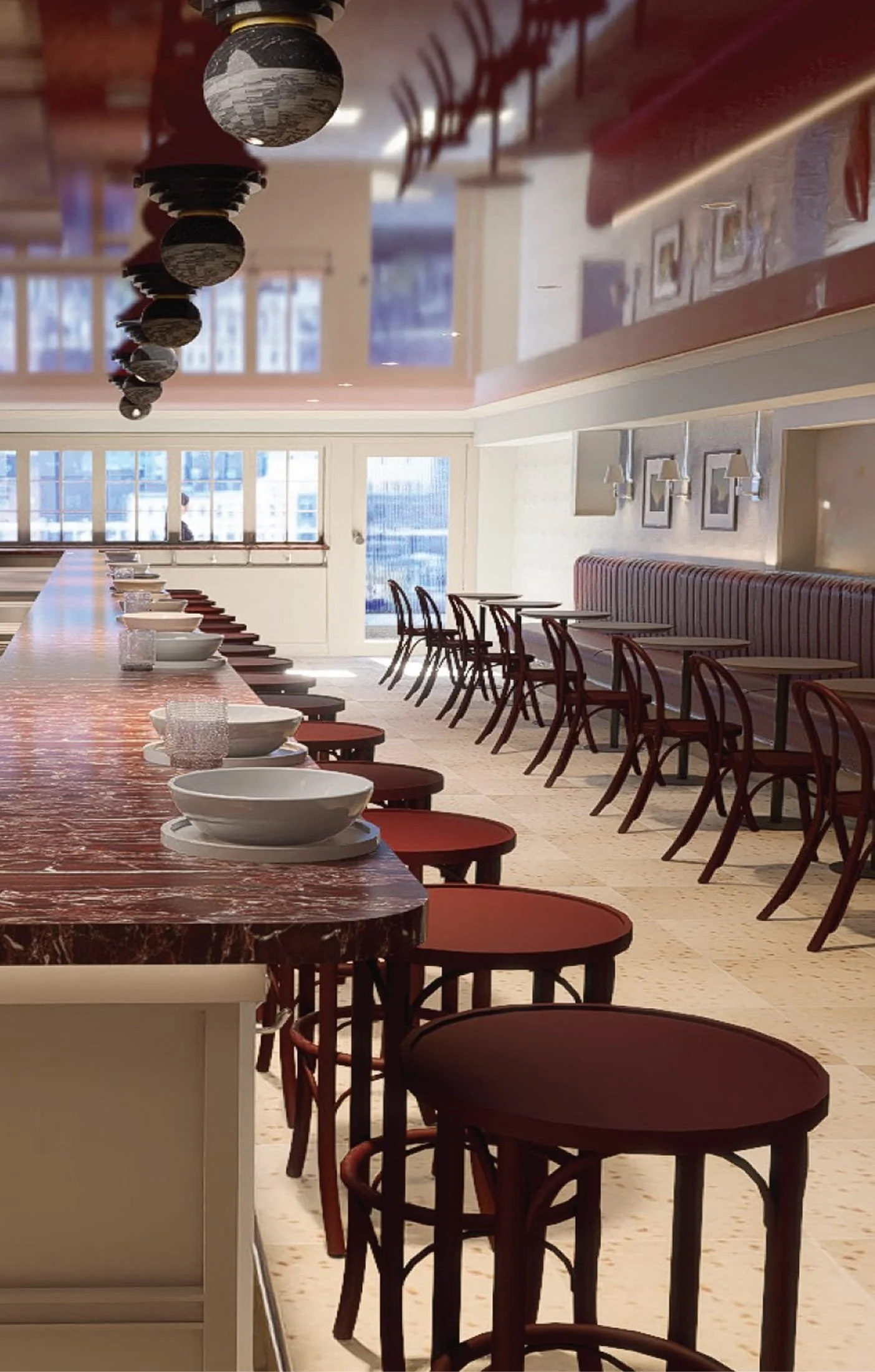 Empty restaurant or cafe with a long marble-topped counter, row of chairs along the counter, and tables with chairs against the wall. Large windows let in natural light.