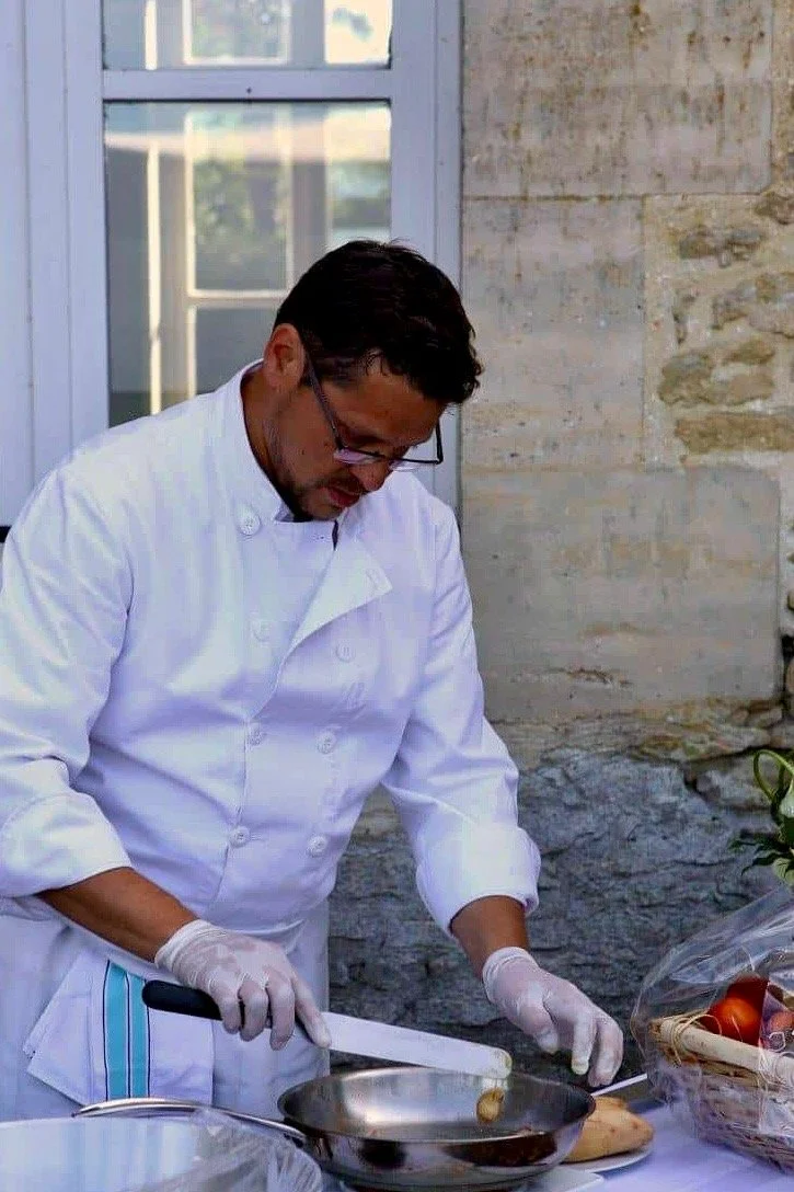 Un chef en robe blanche prépare de la nourriture dans une cuisine lumineuse.