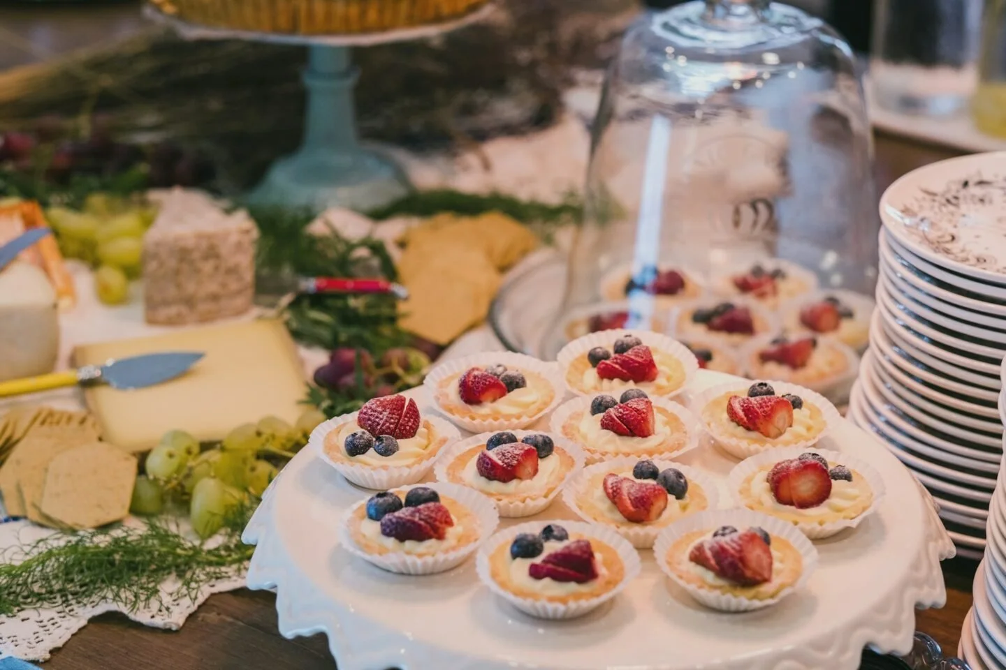 Petits desserts aux fruits rouges présentes sur un plat blanc, entourés d'autres stands de nourriture et de vaisselle.