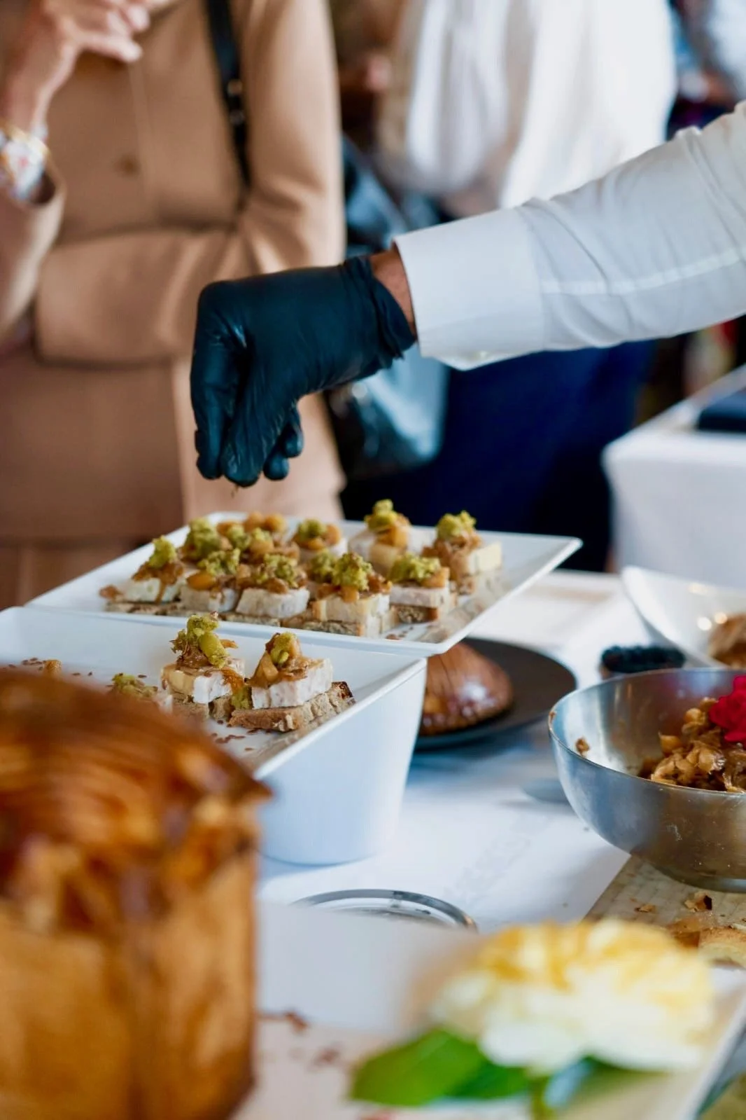 Une main portant un gant noir sert des amuse-gueules sur un plateau lors d'un buffet ou d'un événement social.