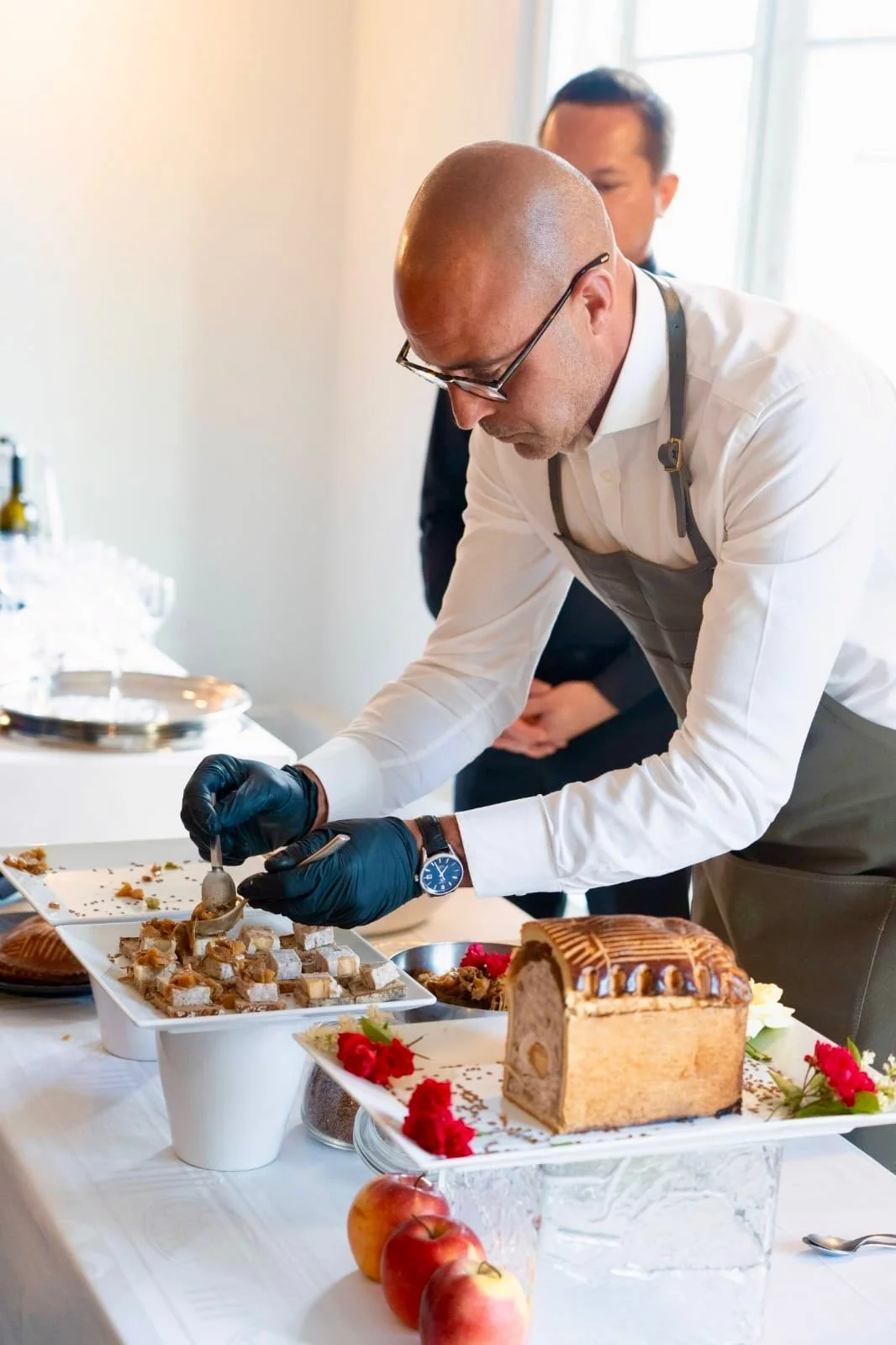 Un chef en train de découper des petits desserts lors d'une réception ou d'un événement, avec un gâteau aux pommes et d'autres amuse-bouches sur la table.