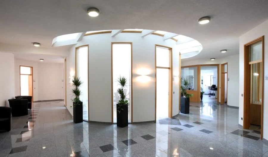 Heller, moderner Büro-Eingangsbereich mit Pflanzen, Fenstern und Sitzgelegenheiten.