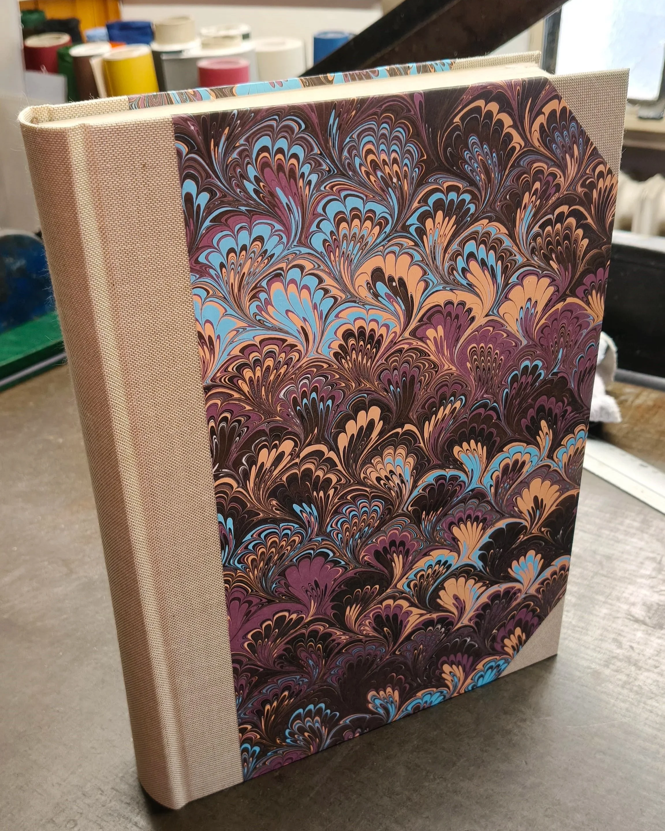 Libro rilegato con copertina in carta fiorentina con sfumature viola, gialle e blu e dorso e angoli in tela grezza